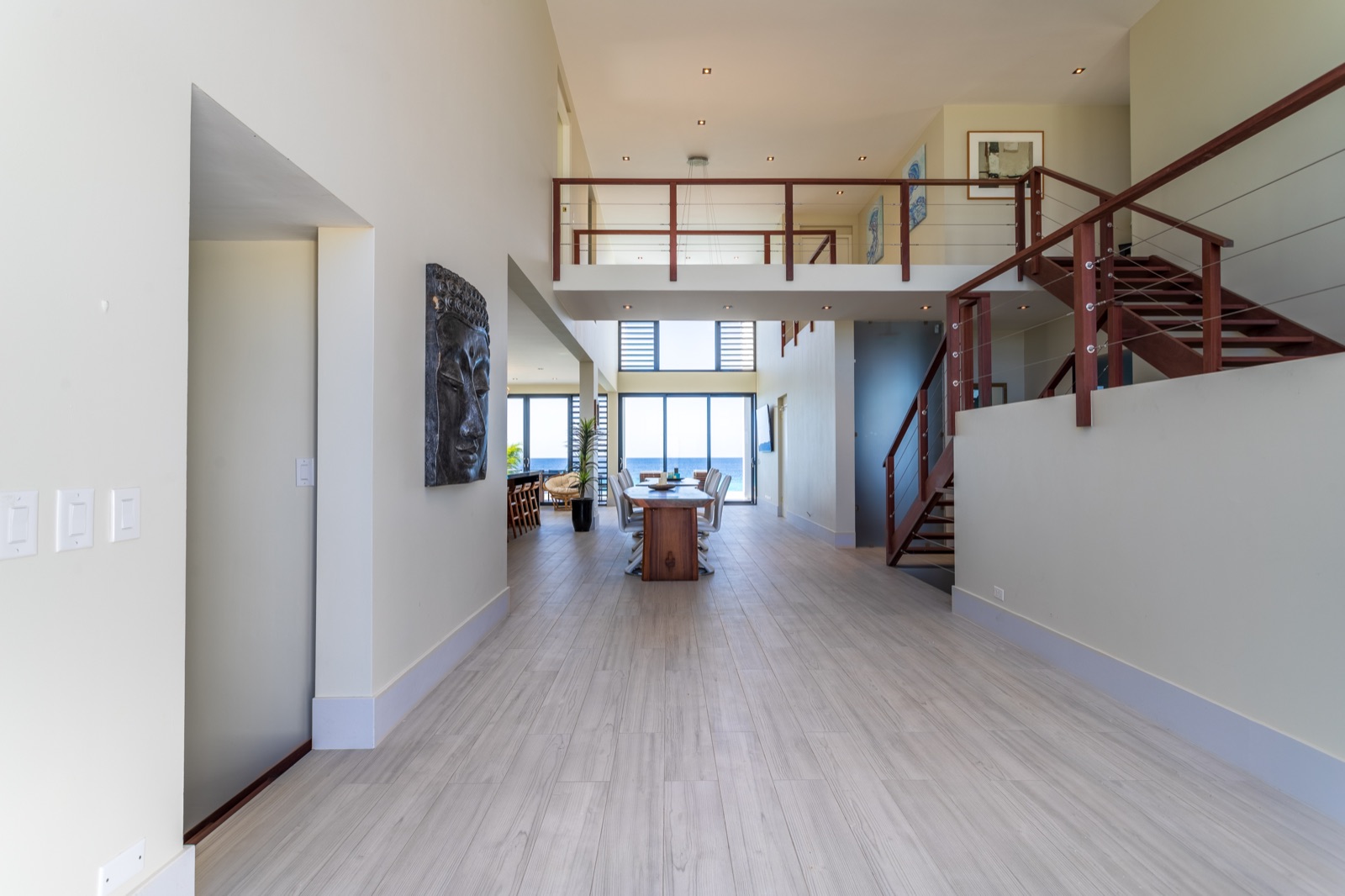 Spacious great room in a luxury Bonaire villa featuring double-height ceilings, a modern wooden staircase, and an oceanfront dining area with floor-to-ceiling windows overlooking the sea.